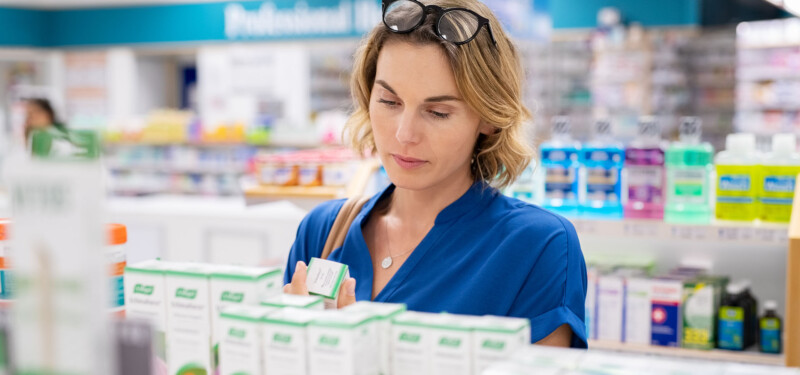 Eine Frau in der Apotheke wählt sorgfältig ein Omega-3-Präparat aus, um das beste Produkt zu finden.